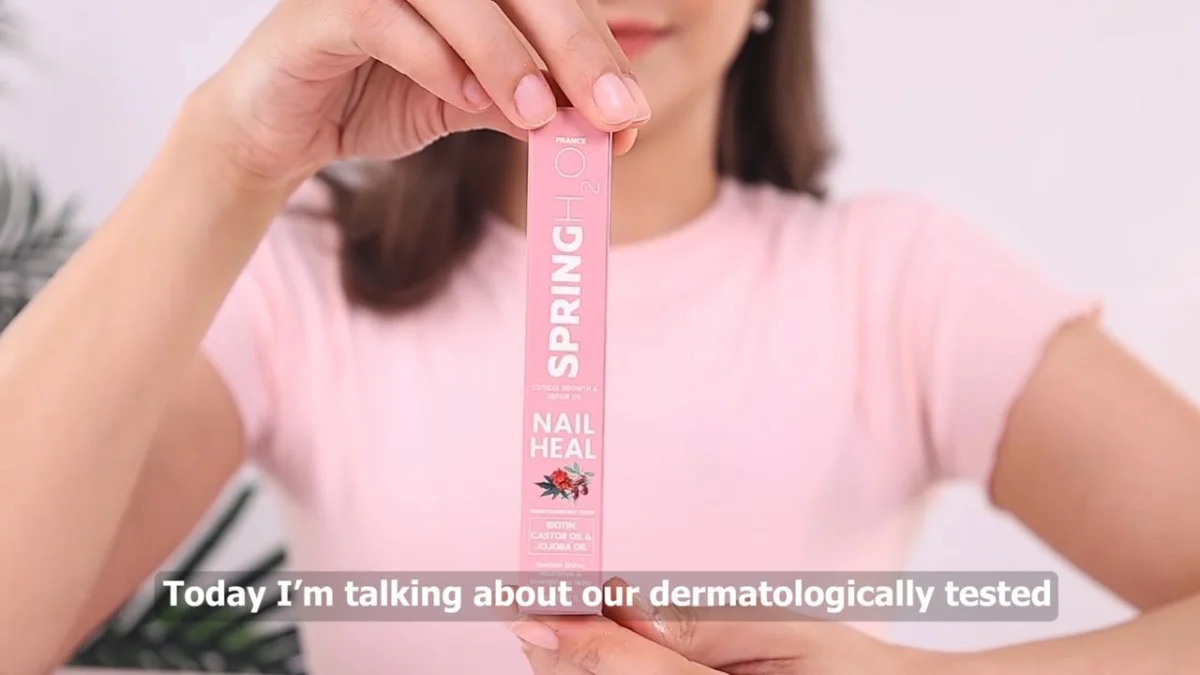 Close-up of an Indian woman creator in a pink top holding a slim pink nail-care oil pack toward the camera with a spoken-line subtitle burned in, the type of talking line where a voiceover patch can avoid a UGC reshoot