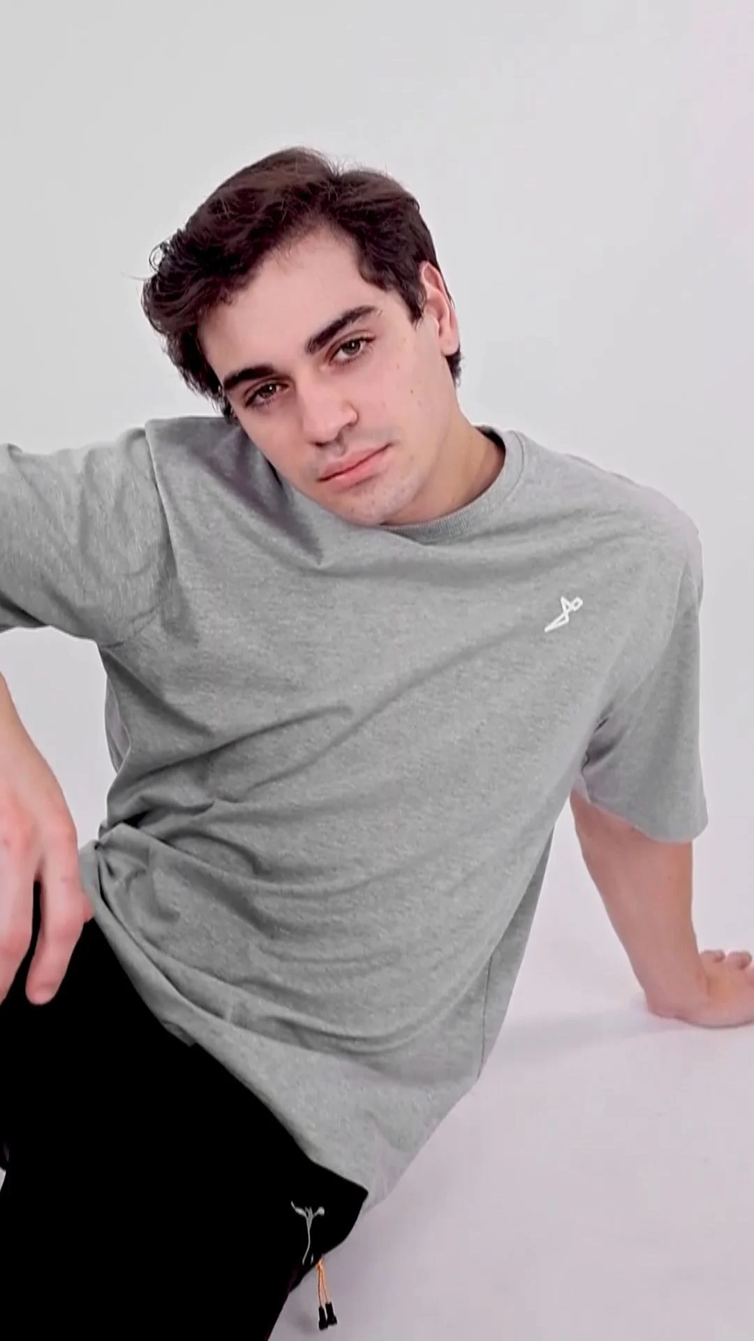 Studio portrait of a male model in a grey T-shirt with the neckline, sleeve and upper-body garment fit visible against a plain background