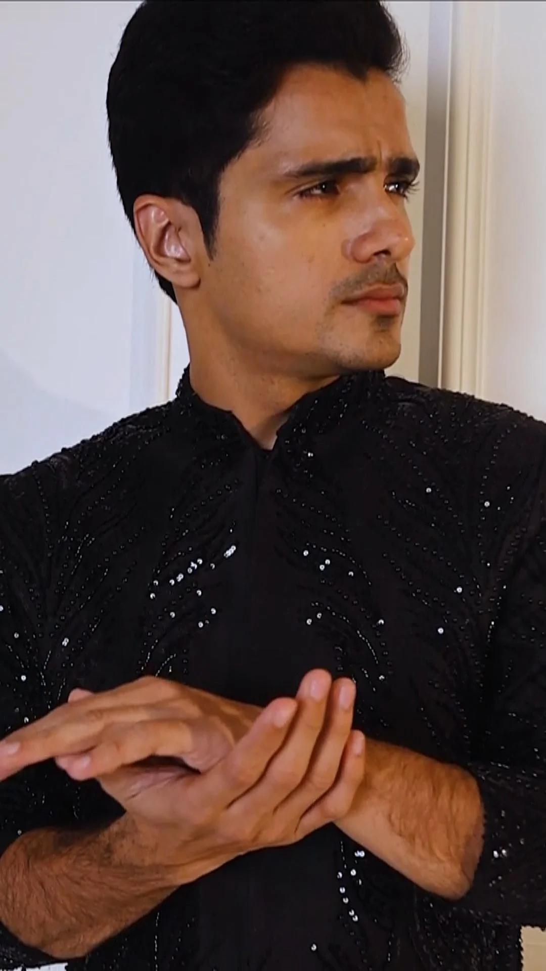Adult male model in a dark textured shirt with hands posed near his chest, illustrating hand placement for a fashion motion brief