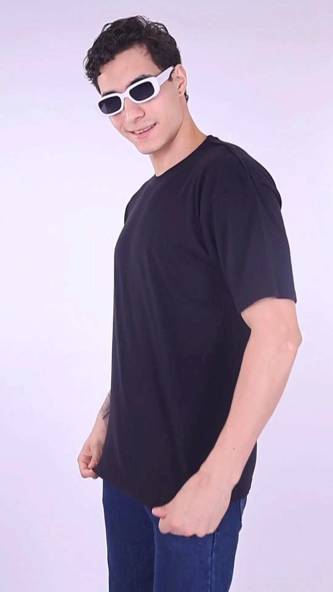 Male model in a plain black T-shirt and dark trousers wearing white sunglasses against a pale studio background