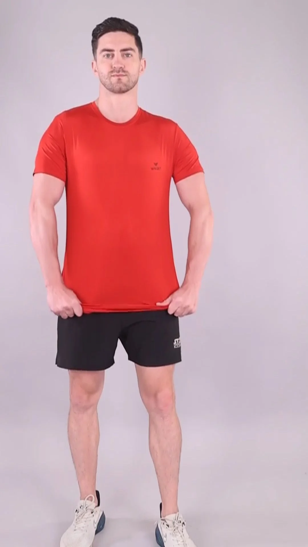 Full-length adult male model in a red T-shirt and dark shorts against a neutral studio background, illustrating current appearance reference