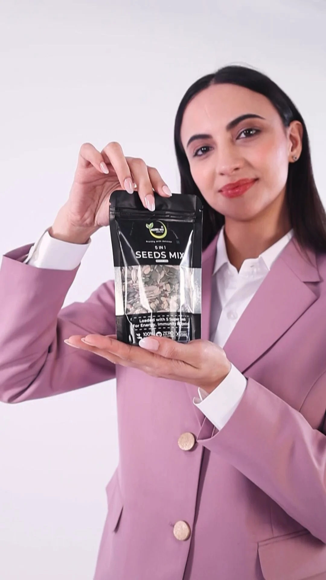 Indian woman in a lilac blazer holding up a pouch of dry fruits to the camera in a vertical 9:16 frame, a working-professional persona for a snack UGC ad concept