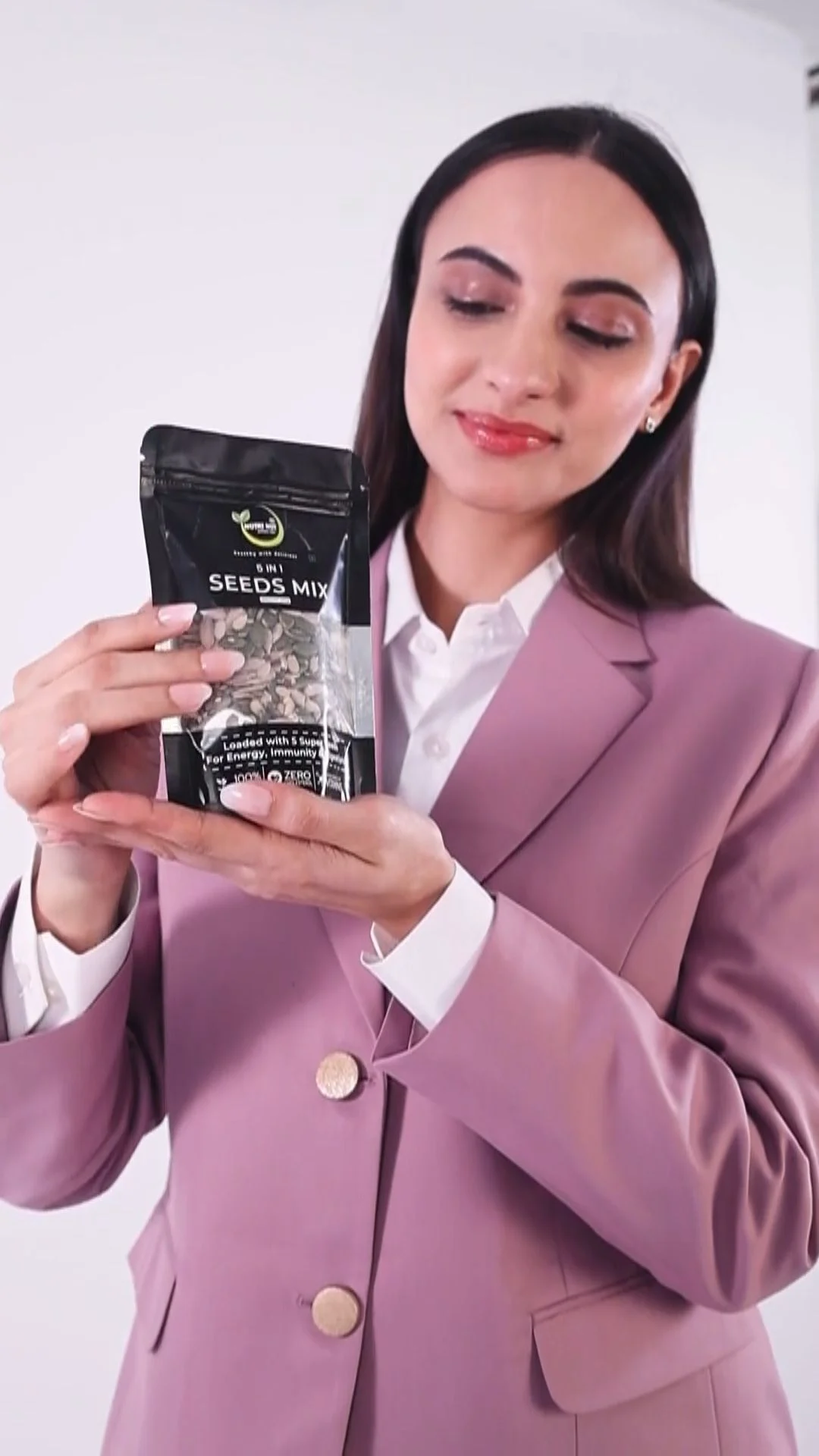 Vertical 9:16 frame of an Indian woman in a pink blazer holding a pouch of seeds at chest height, the product sitting in the safe centre of a 1080x1920 Reels ad