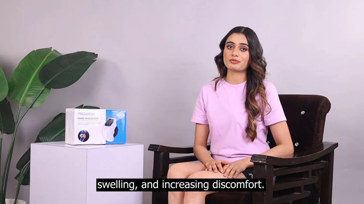Indian presenter in a pink t-shirt seated on a wooden chair explaining a wellness device to camera, burnt-in Hinglish voiceover script subtitle along the bottom of a calm studio set