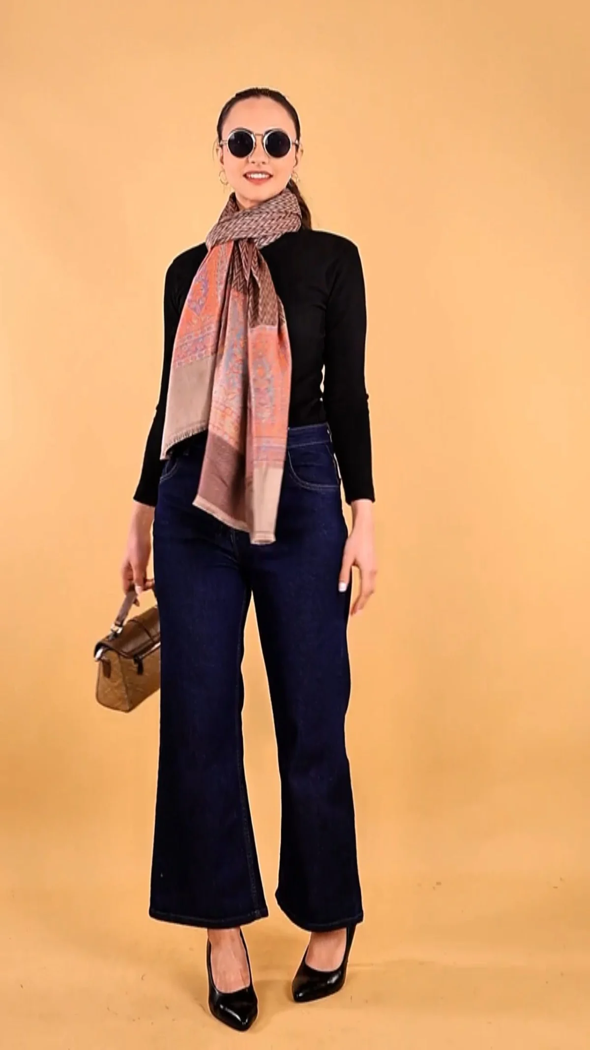 Fashion shoot shot list reference: full-length studio portrait of a woman wearing a muted scarf, dark top and wide-leg trousers against a warm backdrop