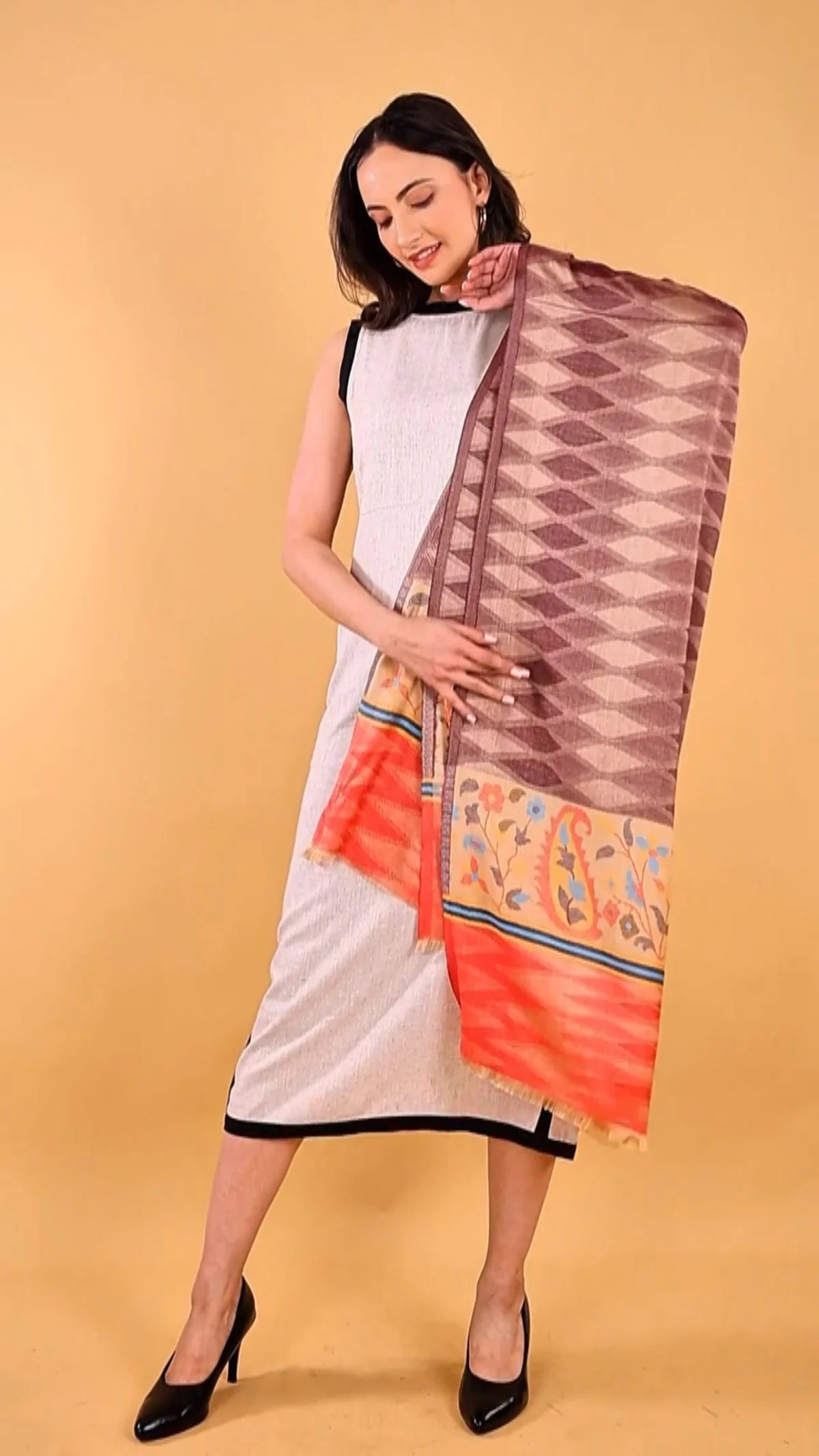 Adult woman holding a patterned stole open over a light dress in a warm studio, showing fabric drape and arm position