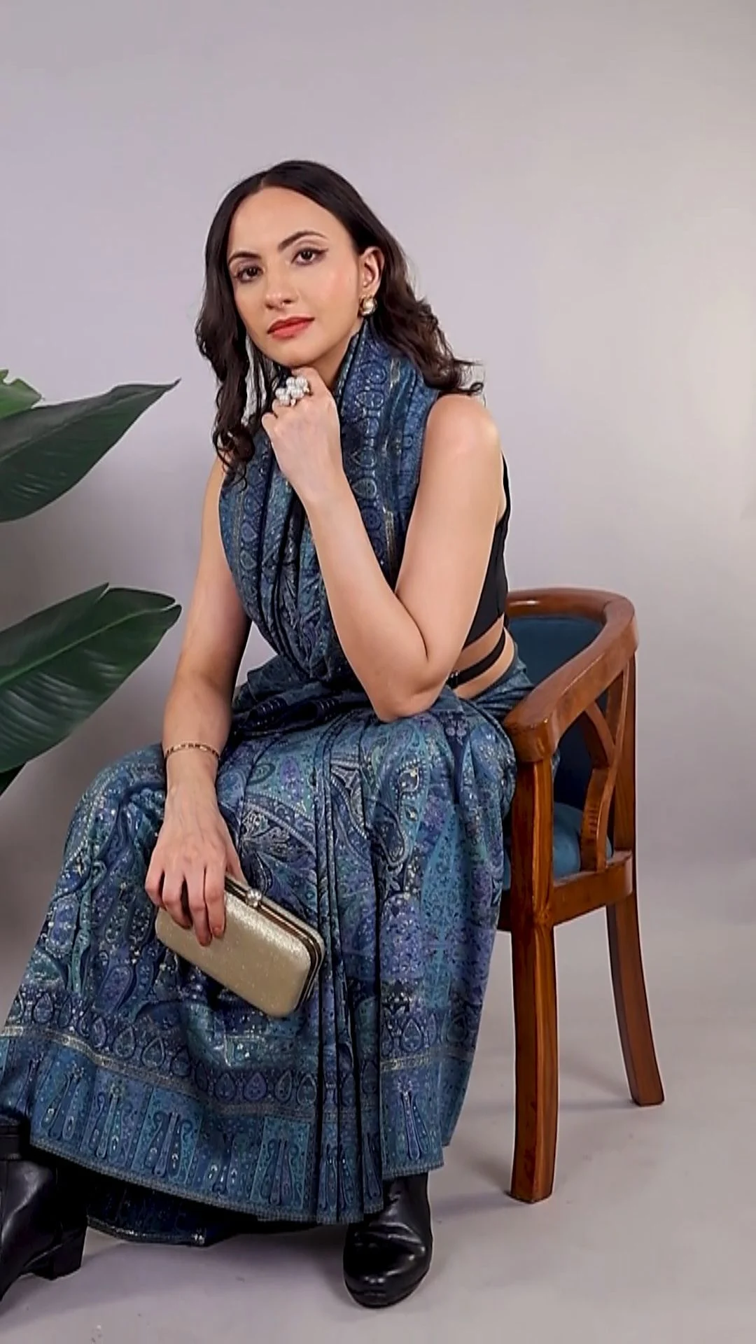 Indian woman in an indigo printed saree seated on a wooden chair in a soft grey studio, holding a gold clutch, the kind of on-camera creator frame a UGC usage rights India contract has to describe before it runs in ads
