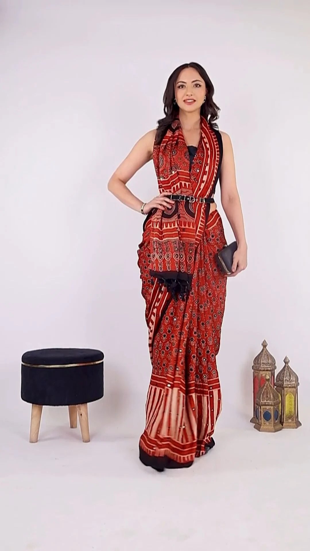Indian female model in a red printed saree posing full-length on a light grey studio set beside a velvet stool and brass lanterns, the kind of on-model catalogue frame a model release form checklist India brands use should cover