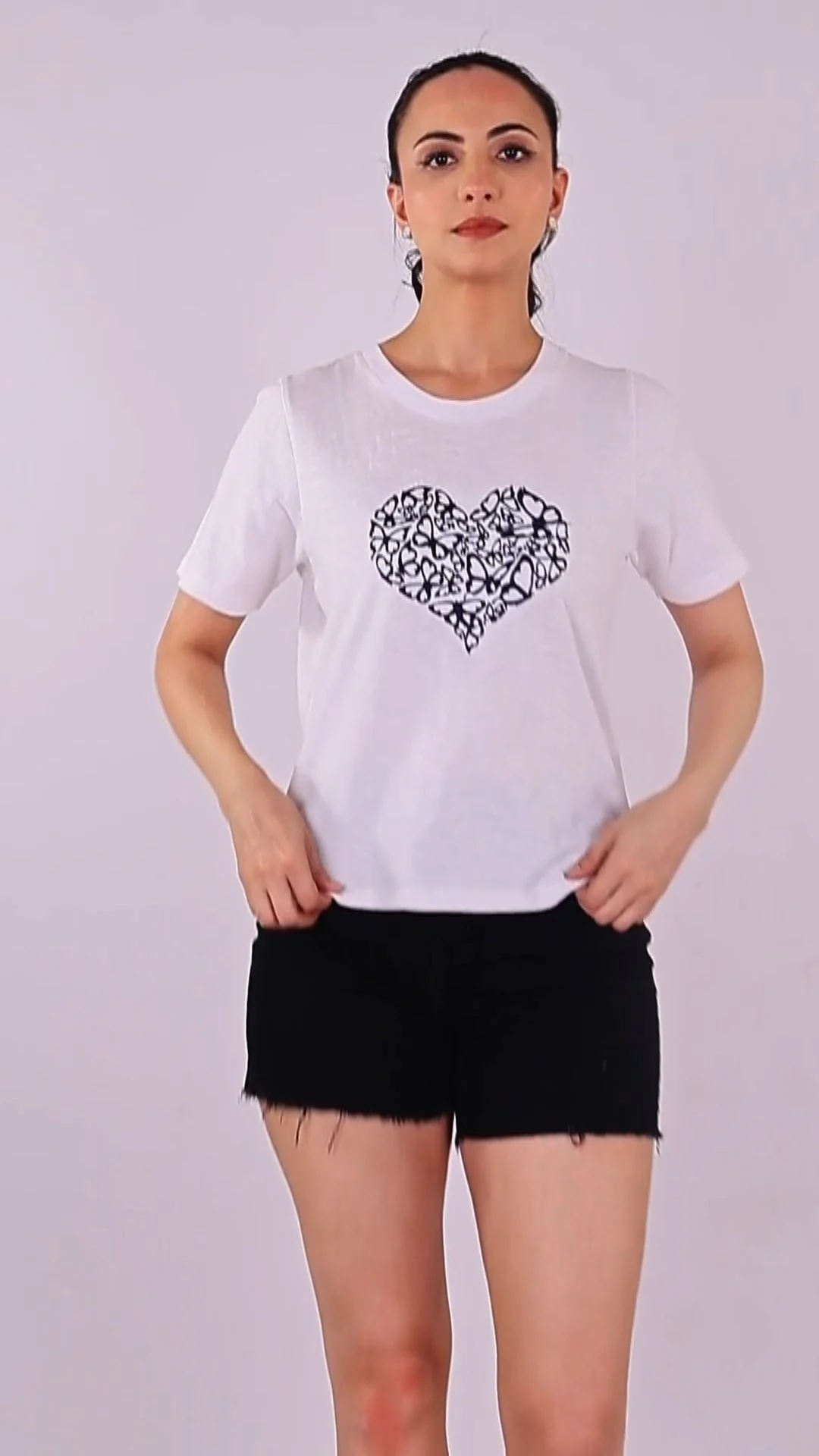 Indian woman model in a white graphic t-shirt and black shorts standing front-facing against a light grey seamless studio backdrop for an Amazon clothing catalogue shoot