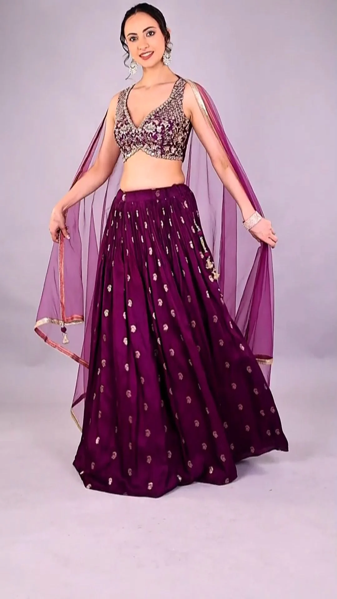Indian woman model in a purple embellished lehenga with a sheer dupatta standing front-facing on a pale studio backdrop for marketplace image exports of ethnic wear