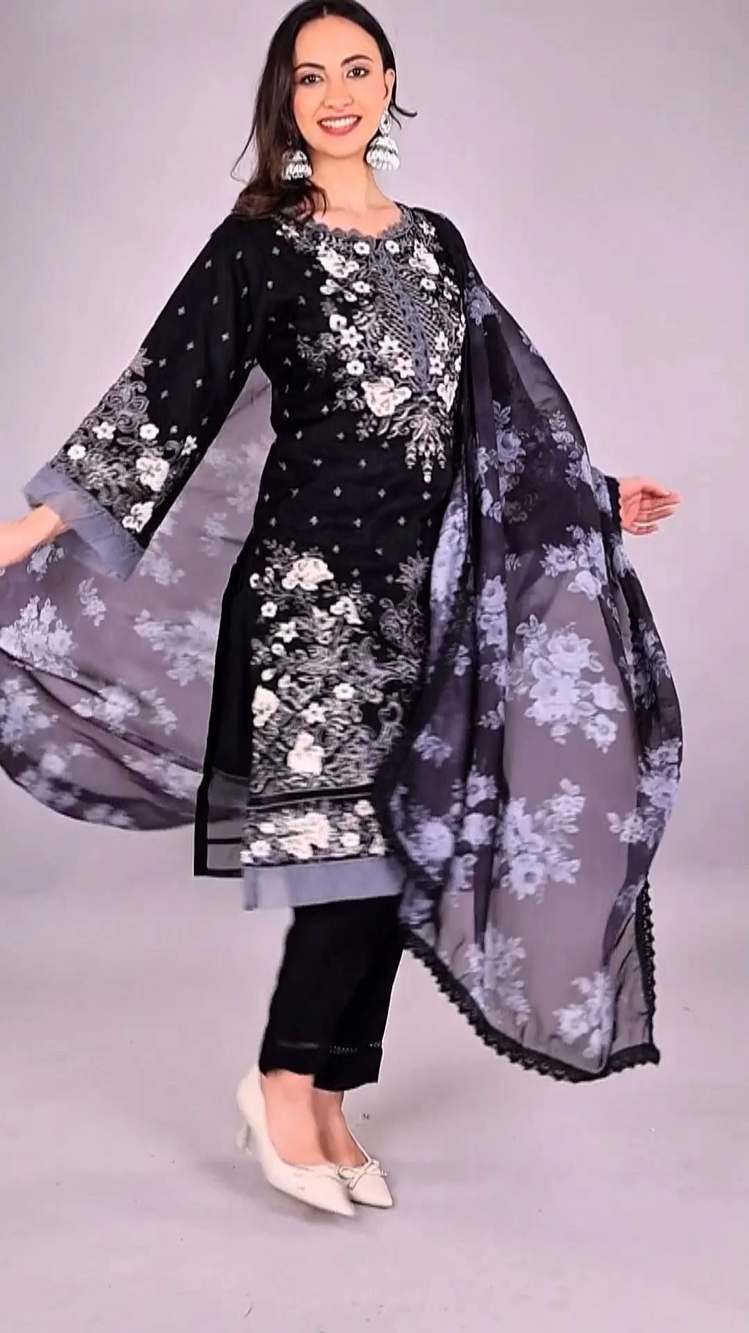 Indian woman model in a black floral printed kurta set with a flowing dupatta mid-movement on a light studio backdrop for a clothing shoot brief
