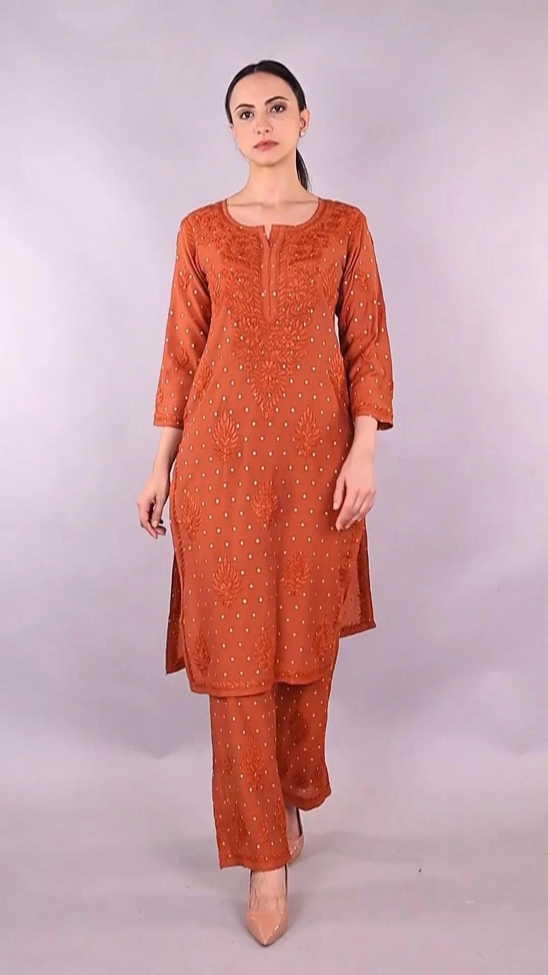 Full-length front view of a young Indian woman in a rust kurta set standing straight against a plain grey studio wall, an example of a clean model portfolio frame
